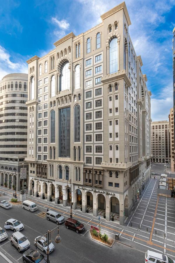 Al Aqeeq Madinah Hotel Medina Exterior foto The photo depicts a large, modern building with a distinctive architectural style. The structure shows a blend of classic and contemporary design elements, featuring ornate details, large glass windows, and a prominent central facade. Surrounding the
