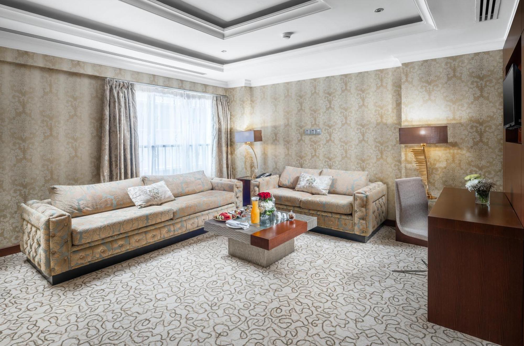 Al Aqeeq Madinah Hotel Medina Exterior foto The photo shows a stylish living room with an elegant design. There are two beige sofas placed opposite each other, adorned with decorative pillows. A low coffee table is positioned in the center, featuring various items, possibly drinks or decorativ
