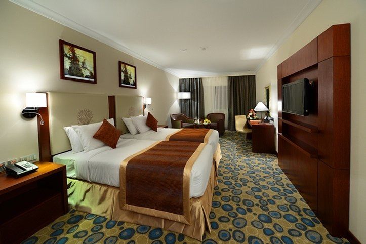 Al Aqeeq Madinah Hotel Medina Exterior foto The photo shows a hotel room featuring two beds with white linens and brown throw blankets. There are decorative pillows on the beds. The room has a modern design, with wooden furniture including bedside tables and a large wooden unit that houses a t